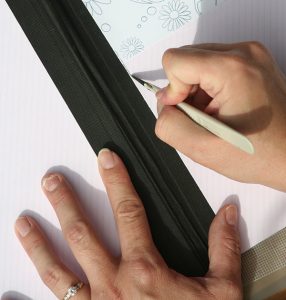 Cutting a slit into the cover of the notebook along the spine to allow ribbon to pass through.